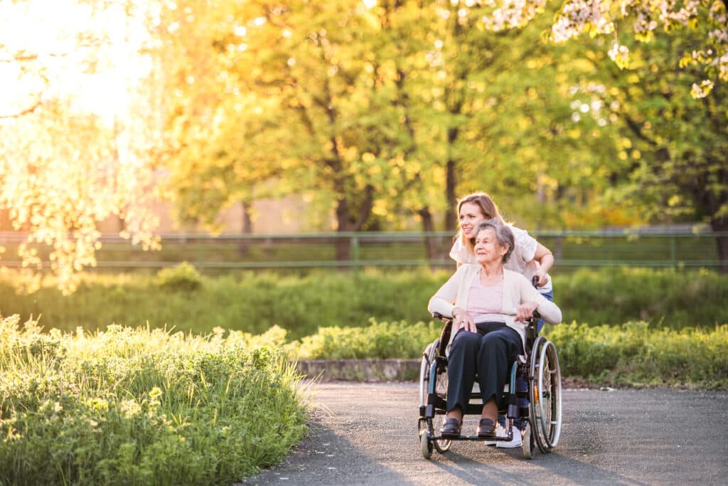 Elderly grandmother in wheelchair with granddaughter in spring nature.